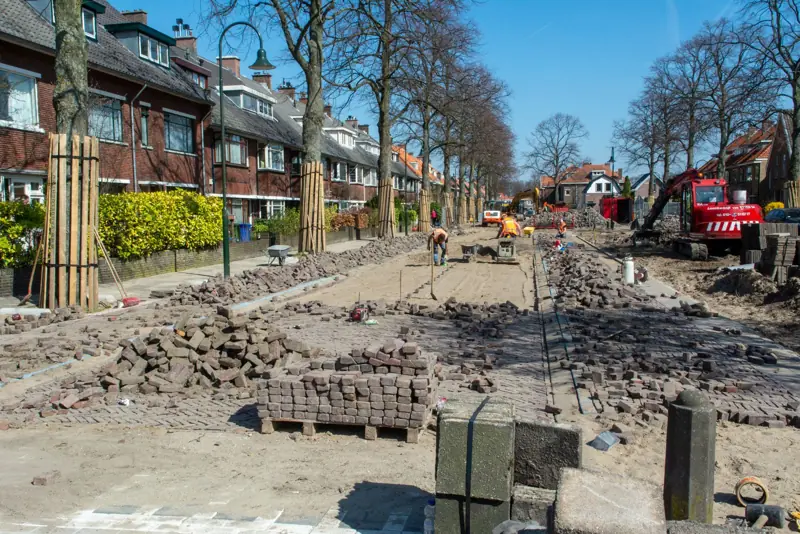 Wegwerker in oranje werkkleding harkt vers asfalt
